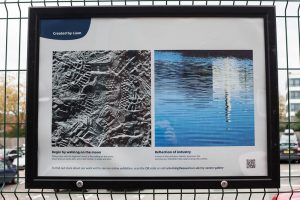One of the posters from the My Severn exhibition at Gloucester Station, showing two photographs taken by participant Liam. In the first, a black and white photograph shows a close up of overlapping footprints on the sand. The second photograph shows the reflection of a building (possibly a factory building from Gloucester docks) in a blue body of water, punctuated by ripples on the water's surface.