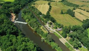 aerial shot over Holt weir and locks showing holt fish pass construction by Unlocking the Severn, Holt Weir, Holt Lock Island and Holt lock. Surrounding trees and farmland in summertime are visible.