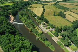 aerial shot over Holt weir and locks showing holt fish pass construction by Unlocking the Severn, Holt Weir, Holt Lock Island and Holt lock. Surrounding trees and farmland in summertime are visible.